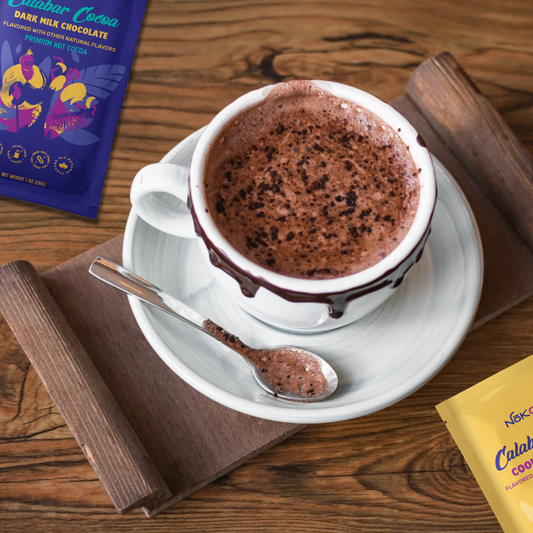 cup of cocoa on a saucer on a wooden table with calabar cocoa packets nearby